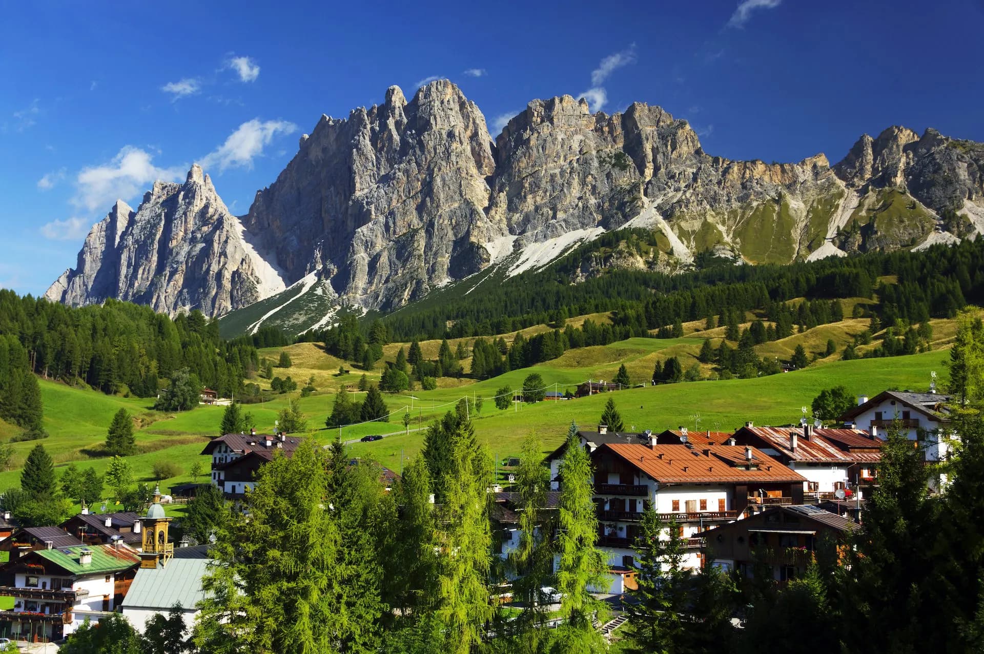 Alpine village with traditional houses below rugged mountains and green meadows in Cortina dAmpezzo surroundings.