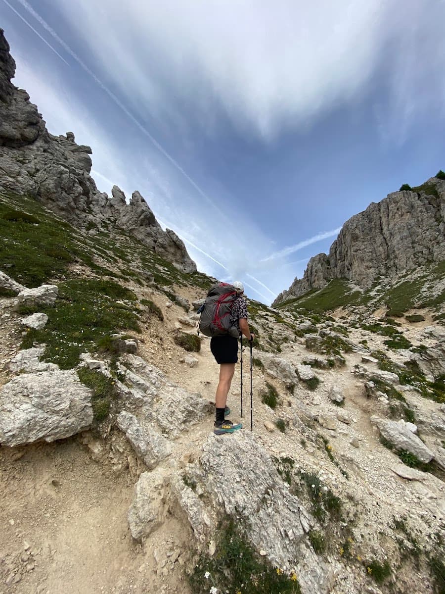 Hiker with backpack and poles on a rocky mountain trail