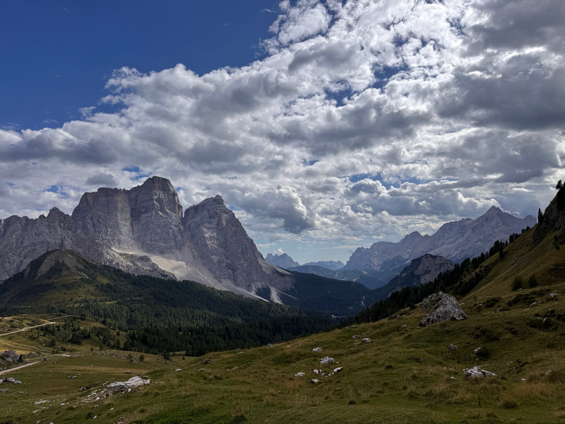 Dolomites mountain massif under dramatic big clouds with green alpine meadows and pine forests