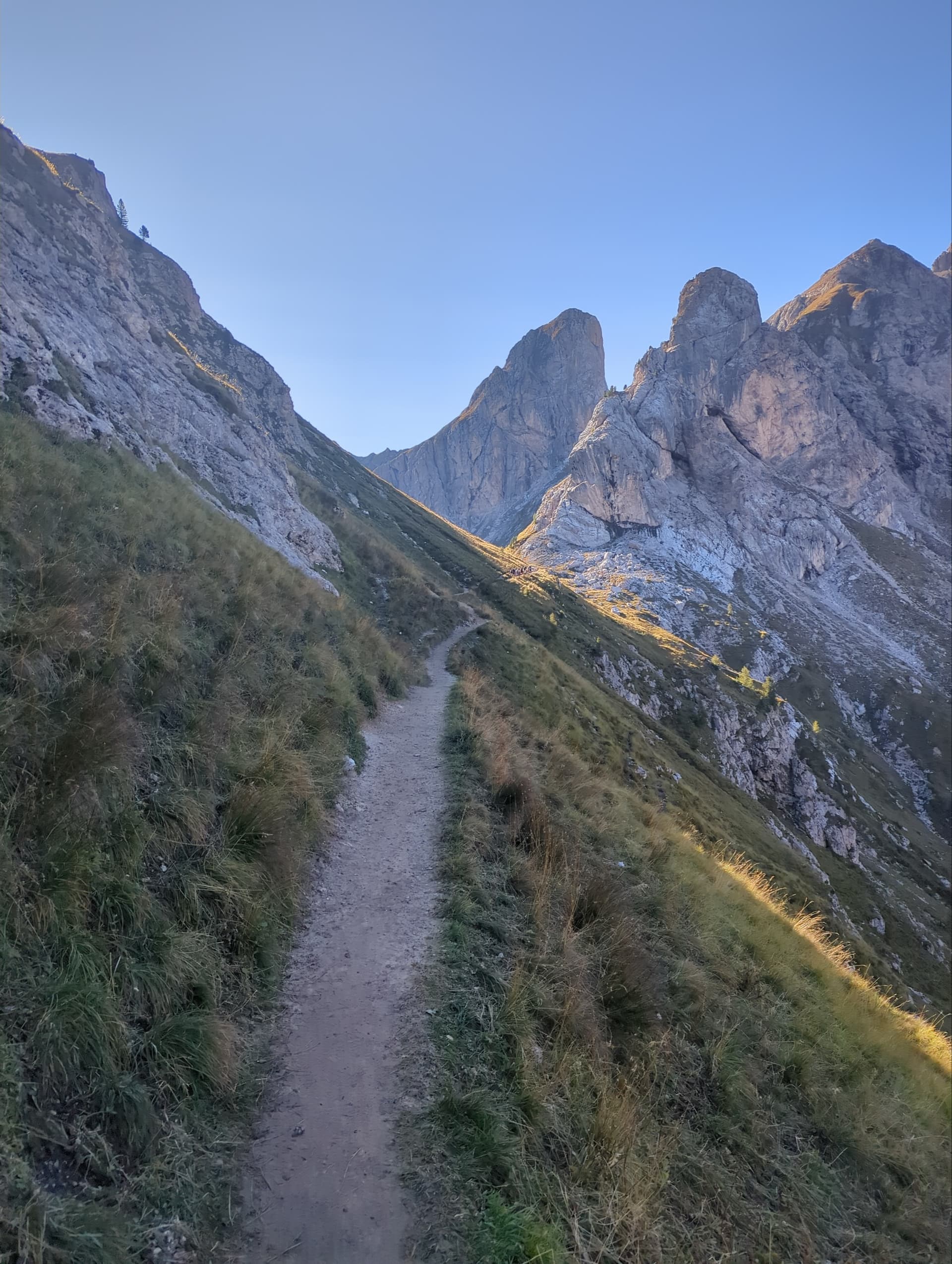 Hiking trail across a grassy alpine slope beneath rocky mountain peaks