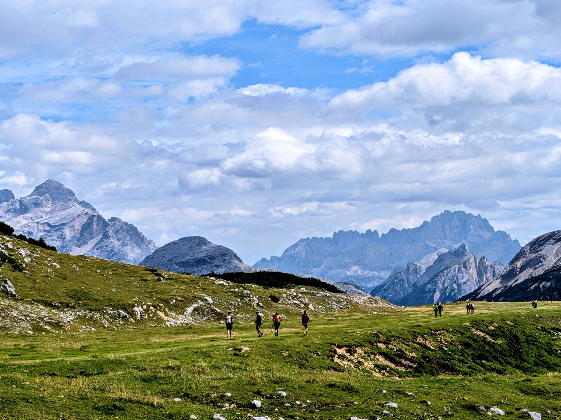 Hikers crossing a high alpine plateau with mountain peaks and cloudy sky