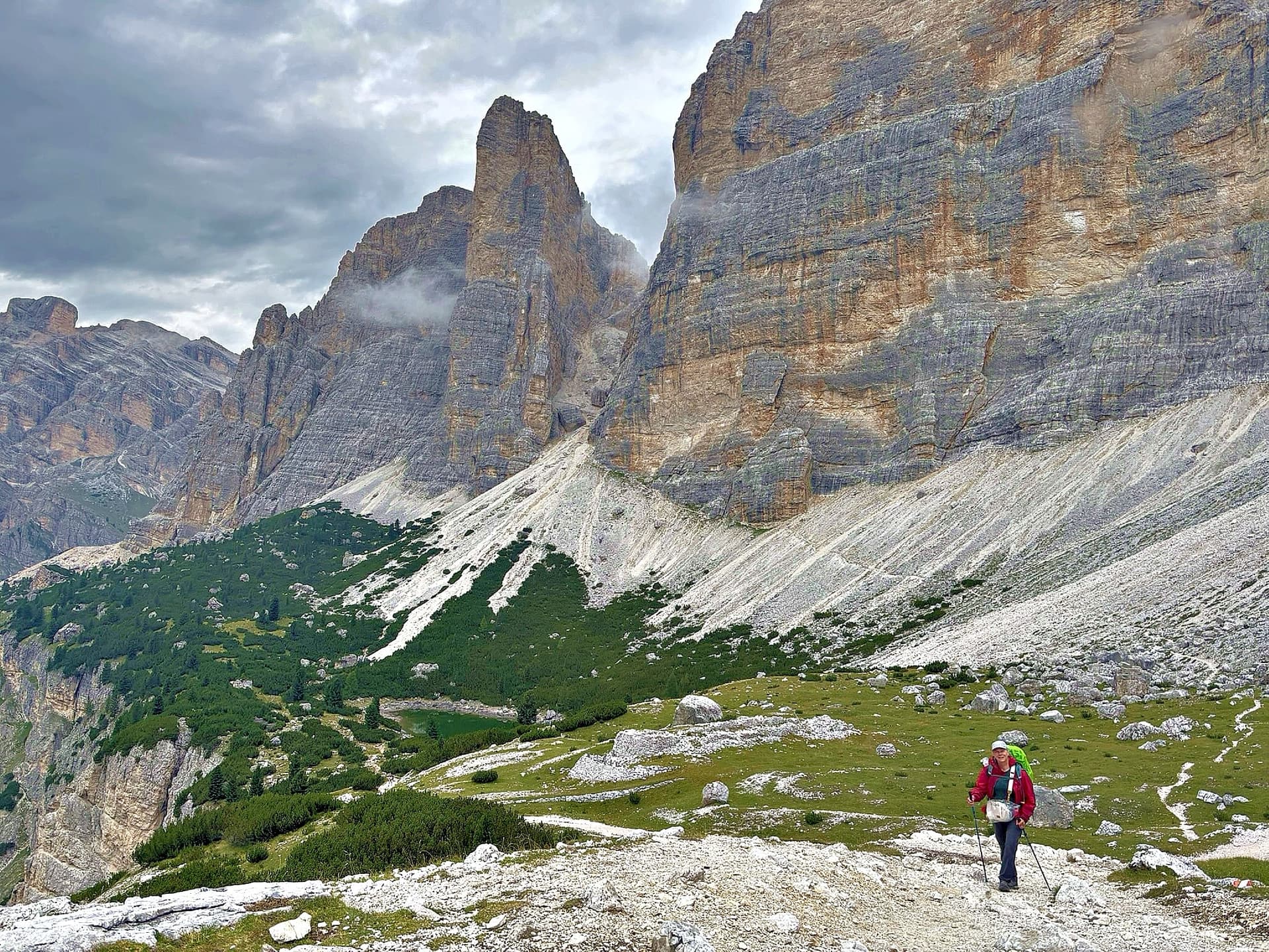 Hiker on rocky mountain trail below towering rock walls
