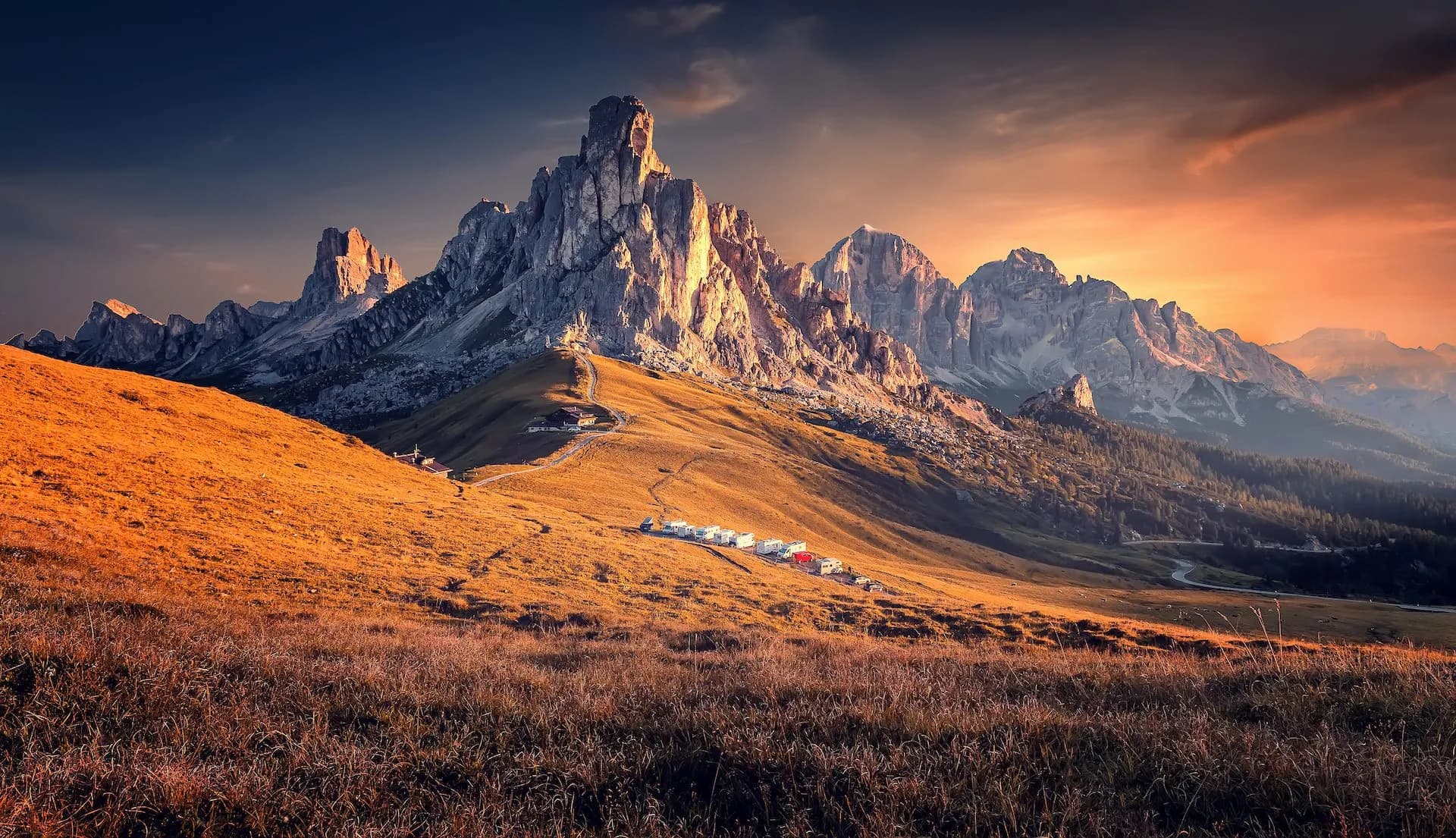Rocky mountain peaks illuminated by sunset over golden grassy slopes at Passo Giau.