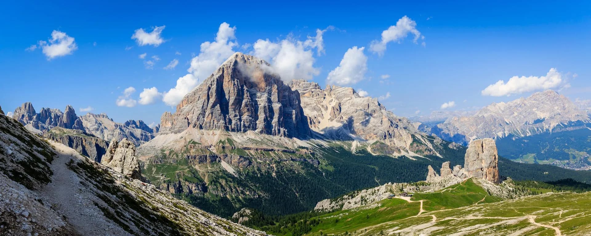 Tofana di Rozes mountain peak with rocky slopes, green meadows, and hiking trails under a blue sky.