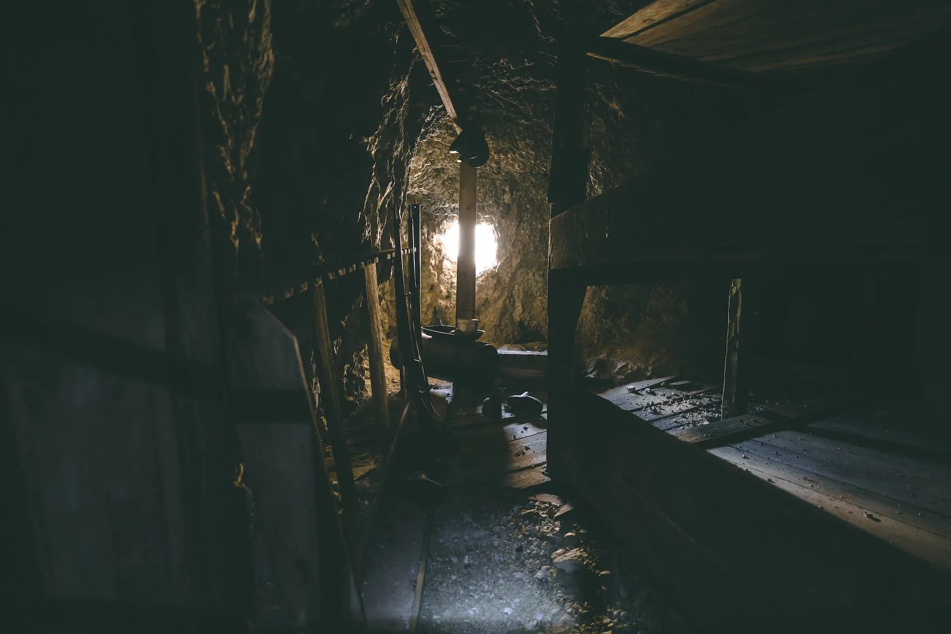 Dark interior of an old mine tunnel with wooden supports and bright light at the end.