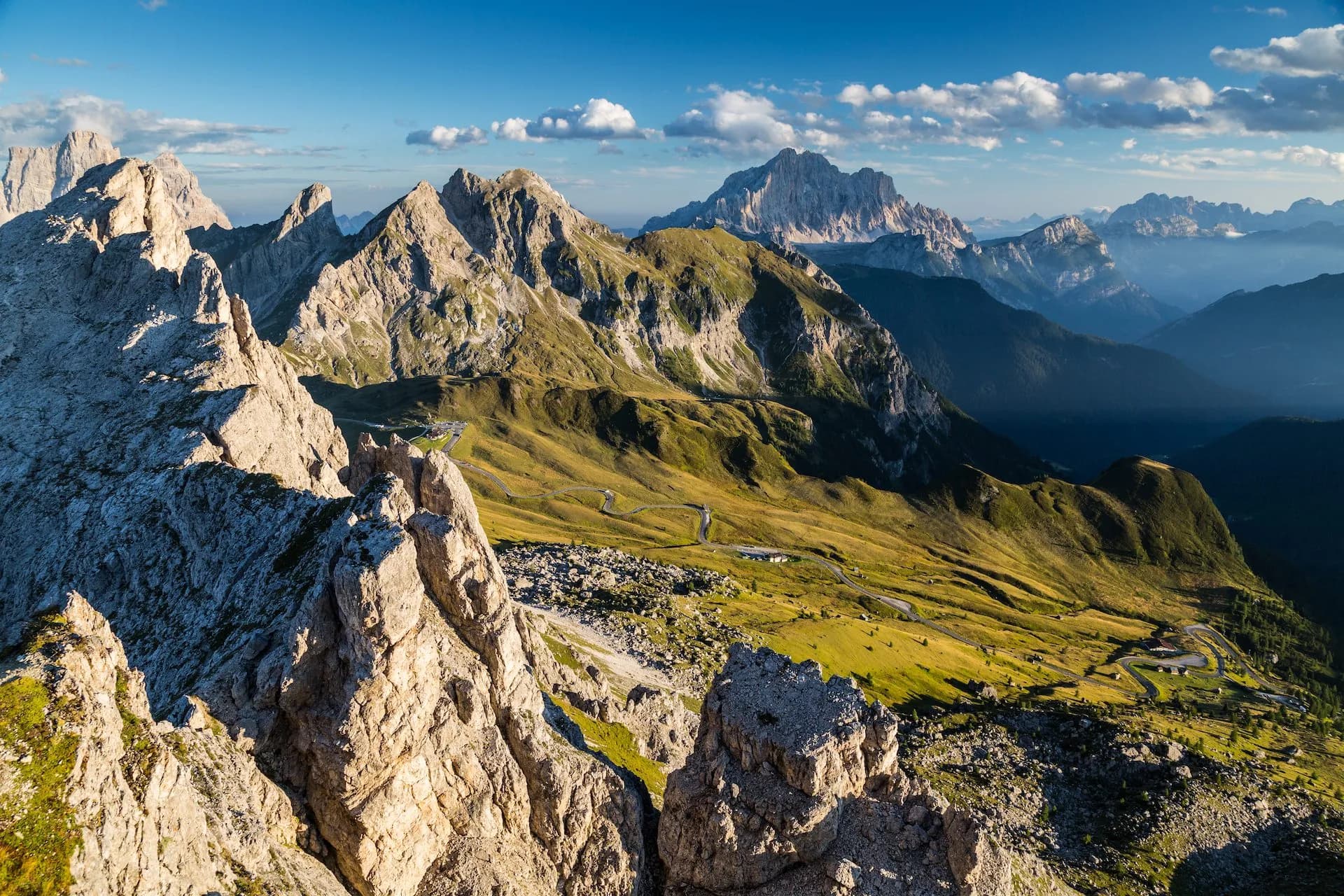 Rocky mountain peaks overlooking green slopes with a winding road at Passo Giau.