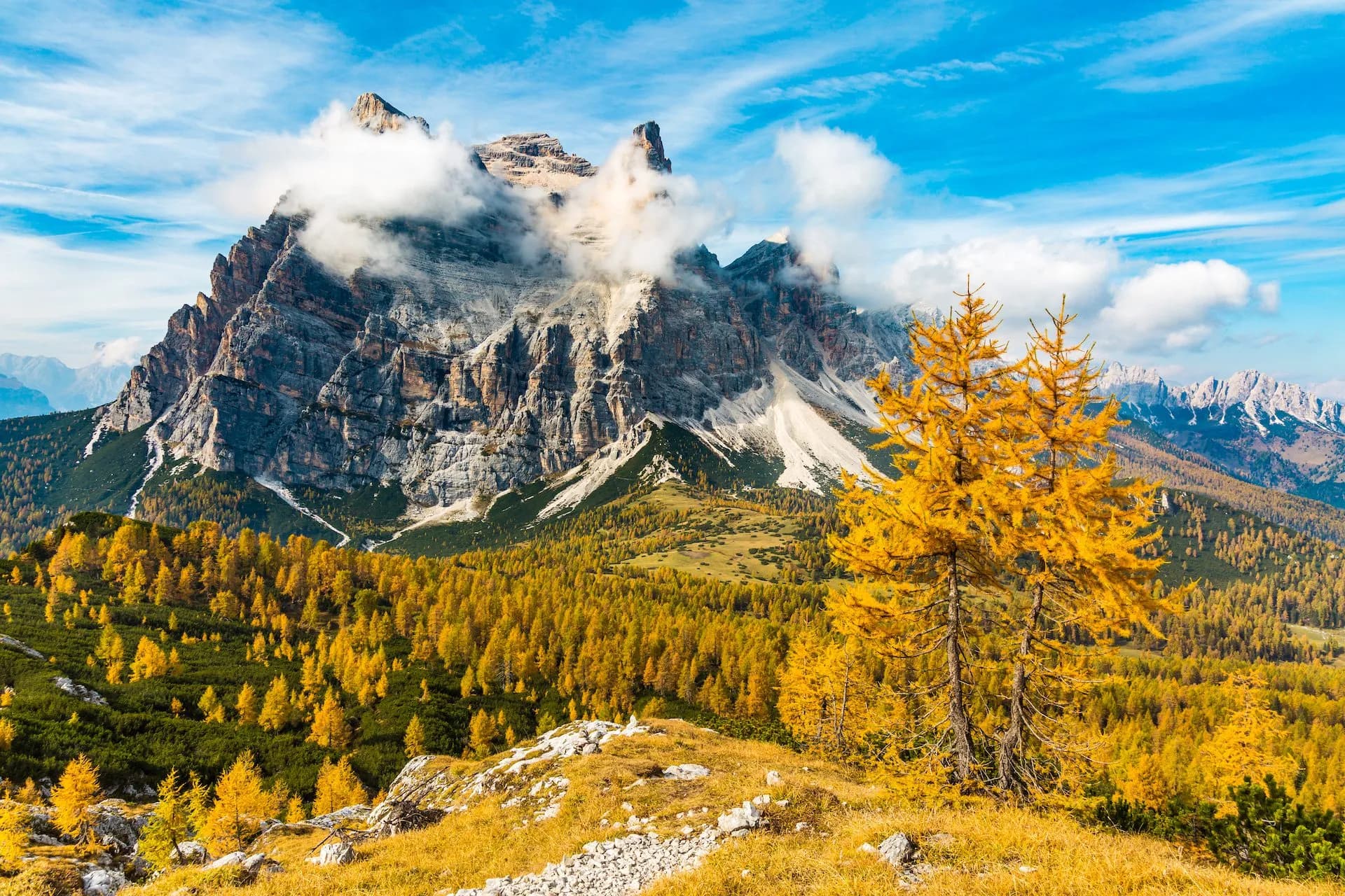 Rugged Monte Pelmo peak with clouds, autumn yellow larches, and blue sky in the Dolomites.