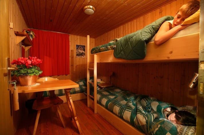 Bunk room with wood paneling, two children sleeping, and a small wooden table with flowers.