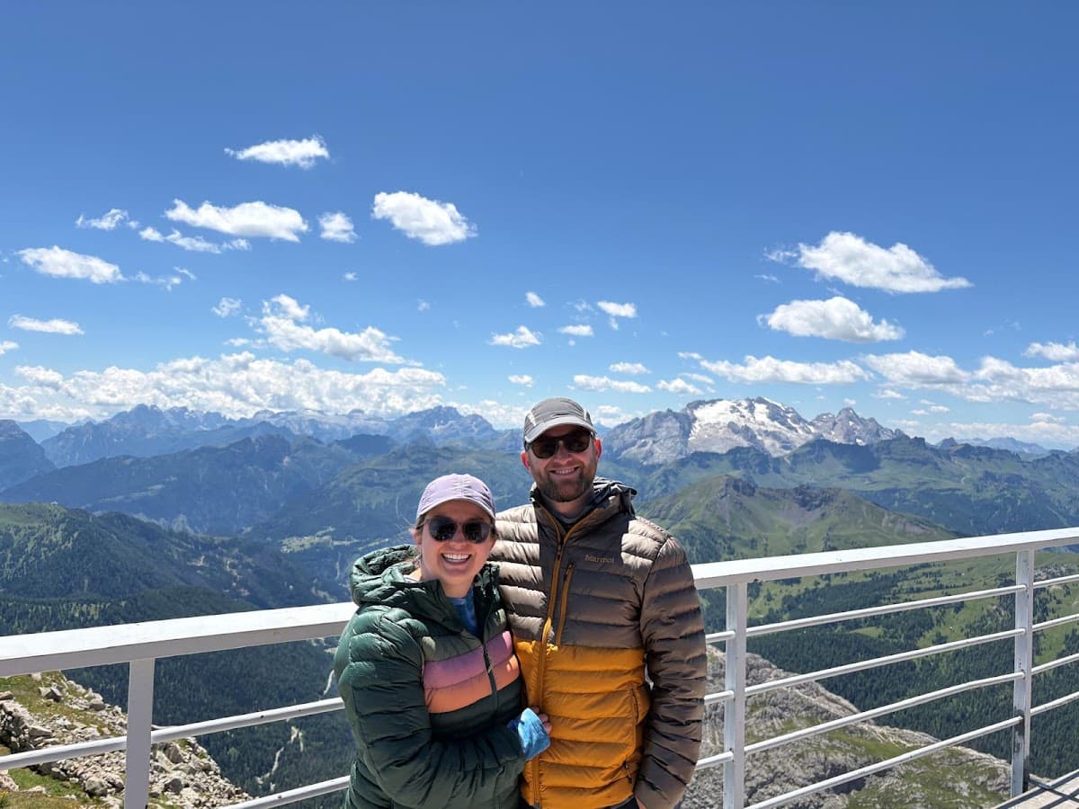 Two hikers posing on a scenic mountain viewpoint with alpine peaks in the background