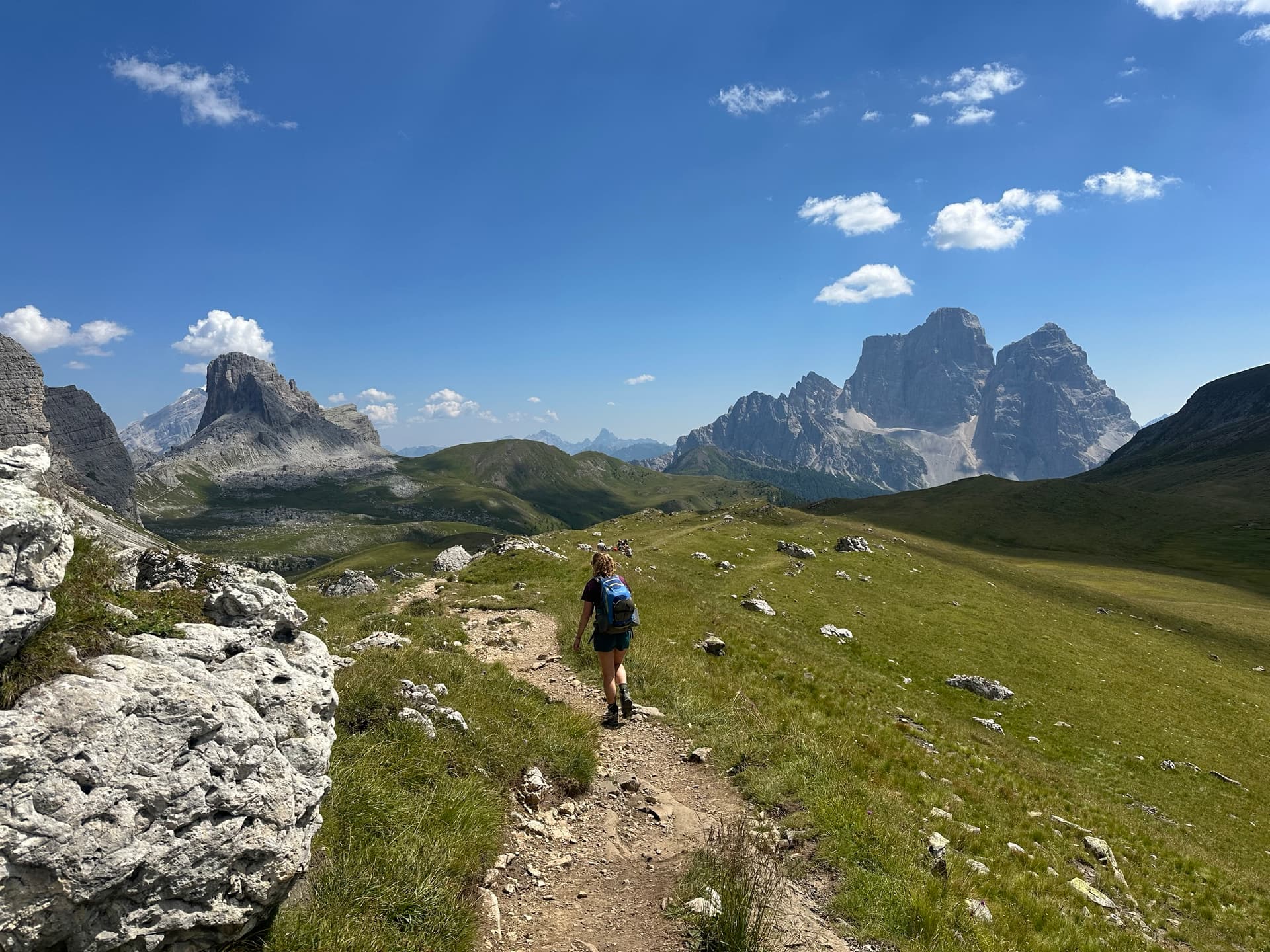 Hiker on dirt trail toward alpine mountain peaks under blue sky